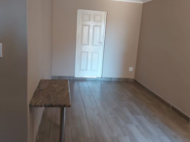 A clean, empty bedroom featuring neutral wall tones, wood-look tiled flooring, and a built-in wall-mounted shelf.