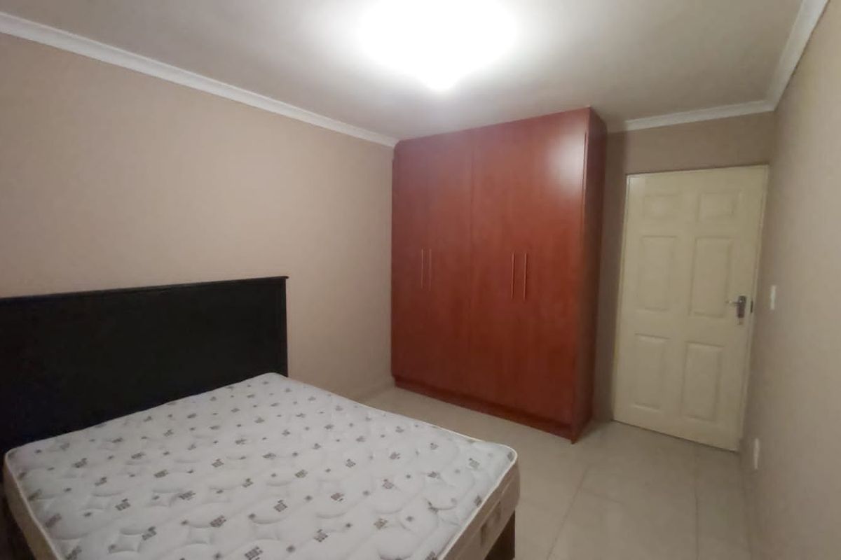 A bedroom featuring tiled flooring, a built-in wooden wardrobe, and neutral wall tones, providing a functional and clean living space.