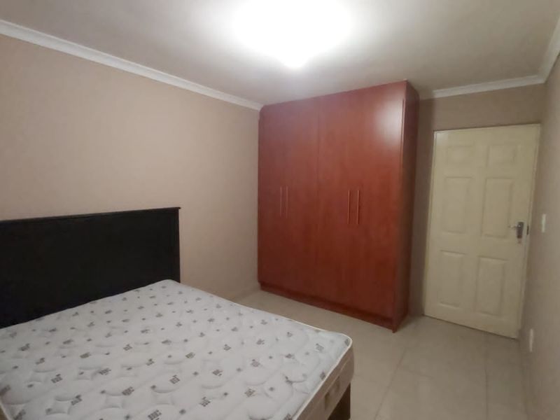A bedroom featuring tiled flooring, a built-in wooden wardrobe, and neutral wall tones, providing a functional and clean living space.