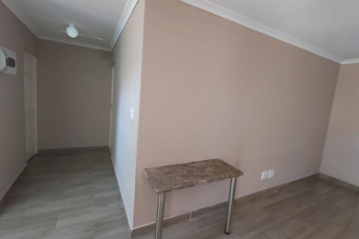 A bright, empty living area featuring neutral wall tones, modern laminate flooring, and clean coving, providing a versatile space for interior design.
