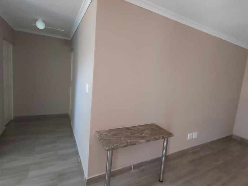 A bright, empty living area featuring neutral wall tones, modern laminate flooring, and clean coving, providing a versatile space for interior design.