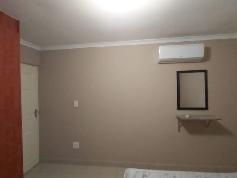 A bedroom featuring a built-in wardrobe, wall-mounted air conditioning unit, and neutral wall finishes.