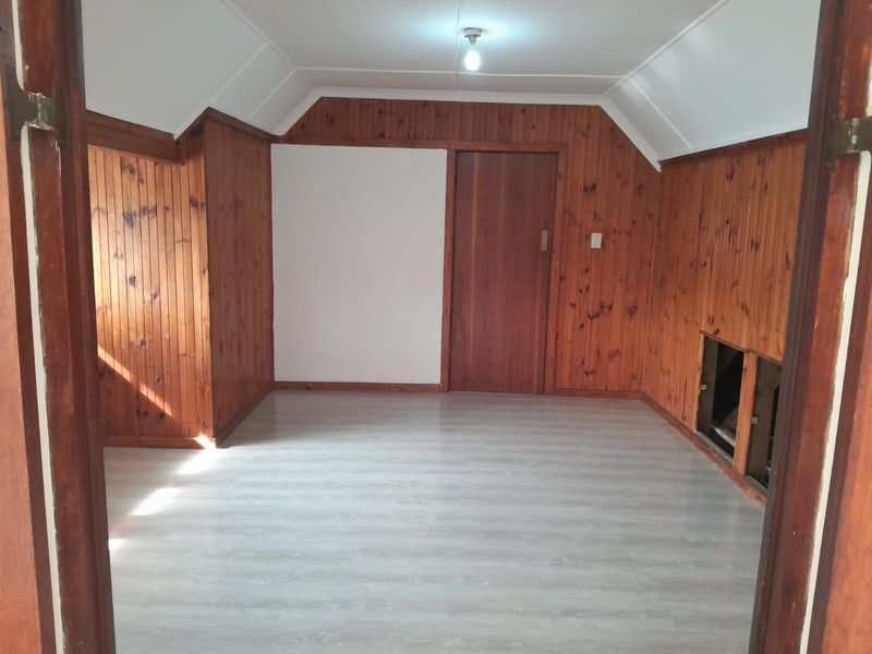 An empty bedroom featuring timber wall paneling, light-toned laminate flooring, and a coved ceiling, currently requiring minor repairs to the wall paneling.