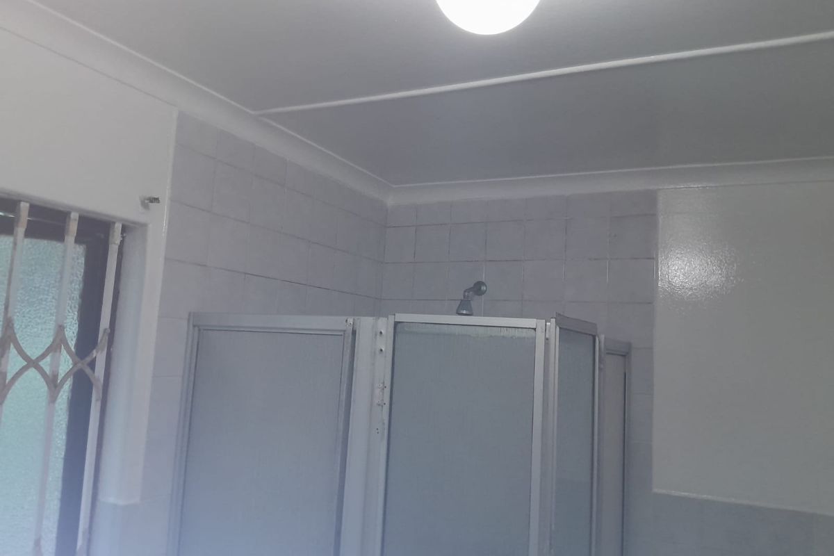 A functional bathroom featuring a shower enclosure with tiled walls and a security gate on the window.