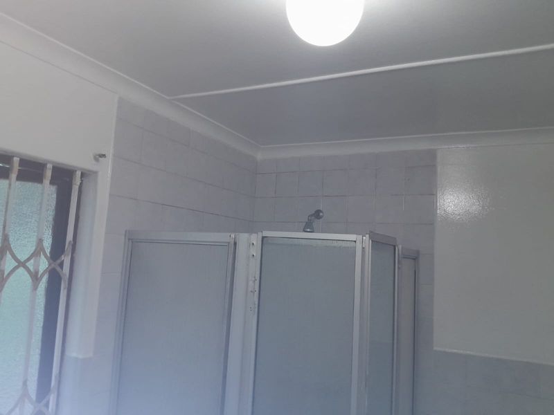 A functional bathroom featuring a shower enclosure with tiled walls and a security gate on the window.