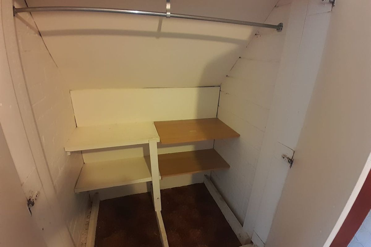 A small utility storage closet featuring built-in shelving and a hanging rail, suitable for additional household storage.
