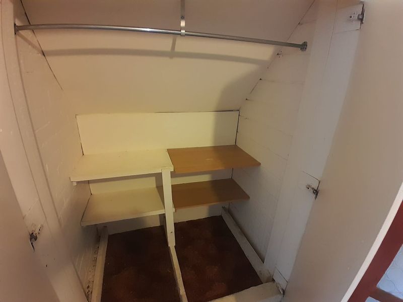 A small utility storage closet featuring built-in shelving and a hanging rail, suitable for additional household storage.