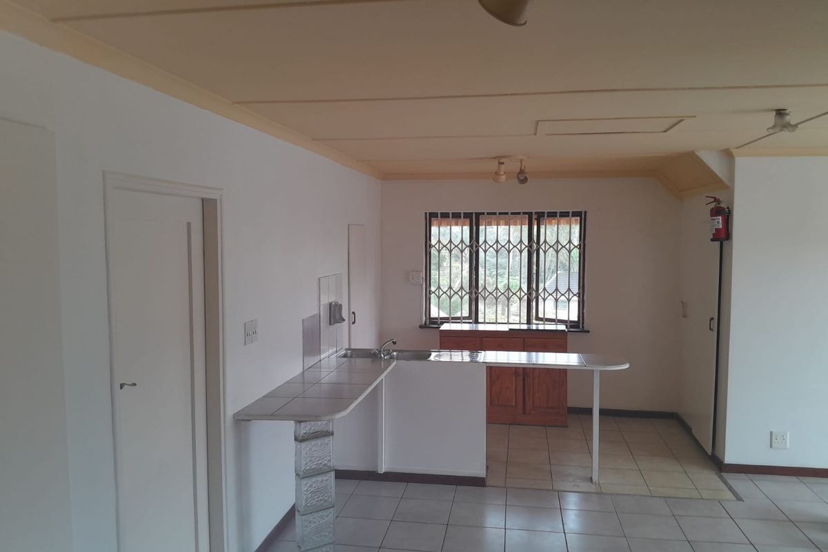 A functional kitchen area featuring tiled countertops, a breakfast bar with a glass block support, and tiled flooring in a neutral, open-plan layout.