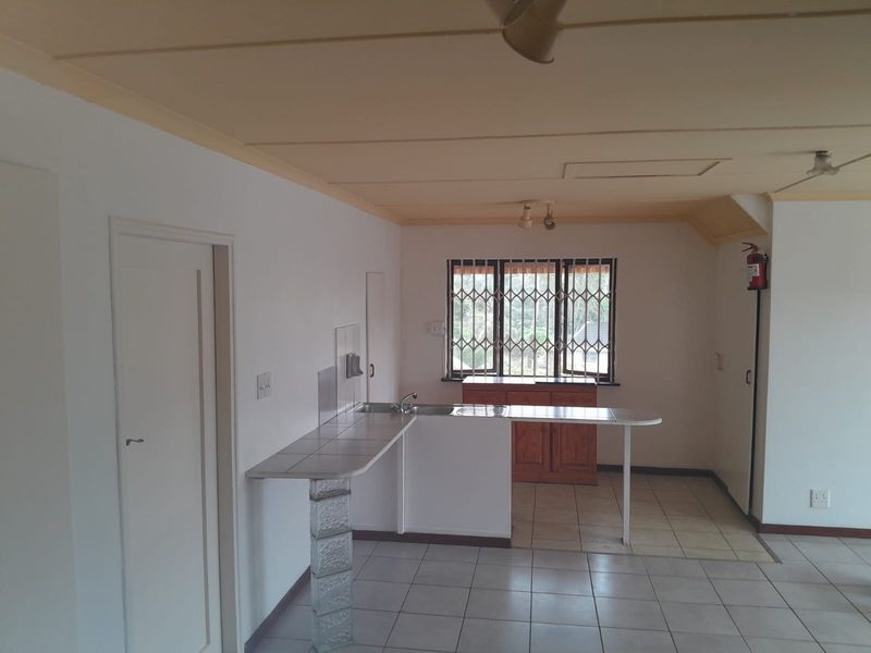 A functional kitchen area featuring tiled countertops, a breakfast bar with a glass block support, and tiled flooring in a neutral, open-plan layout.