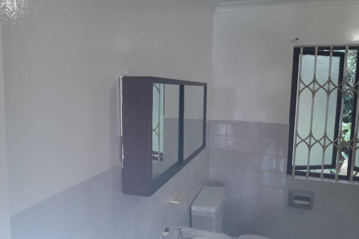 A functional bathroom featuring a wall-mounted medicine cabinet, standard toilet, and washbasin with tiled walls and a security-gated window.