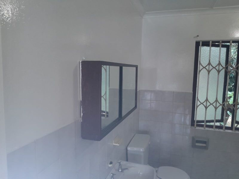 A functional bathroom featuring a wall-mounted medicine cabinet, standard toilet, and washbasin with tiled walls and a security-gated window.