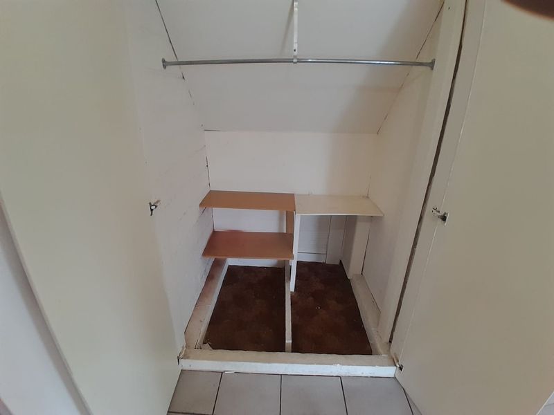 A small utility storage closet featuring built-in shelving and a hanging rail, currently showing signs of wear and a missing floor section.