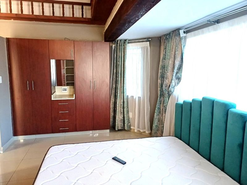 A well-maintained bedroom featuring built-in wooden cupboards, tiled flooring, and exposed timber ceiling beams, offering a cozy and functional living space.