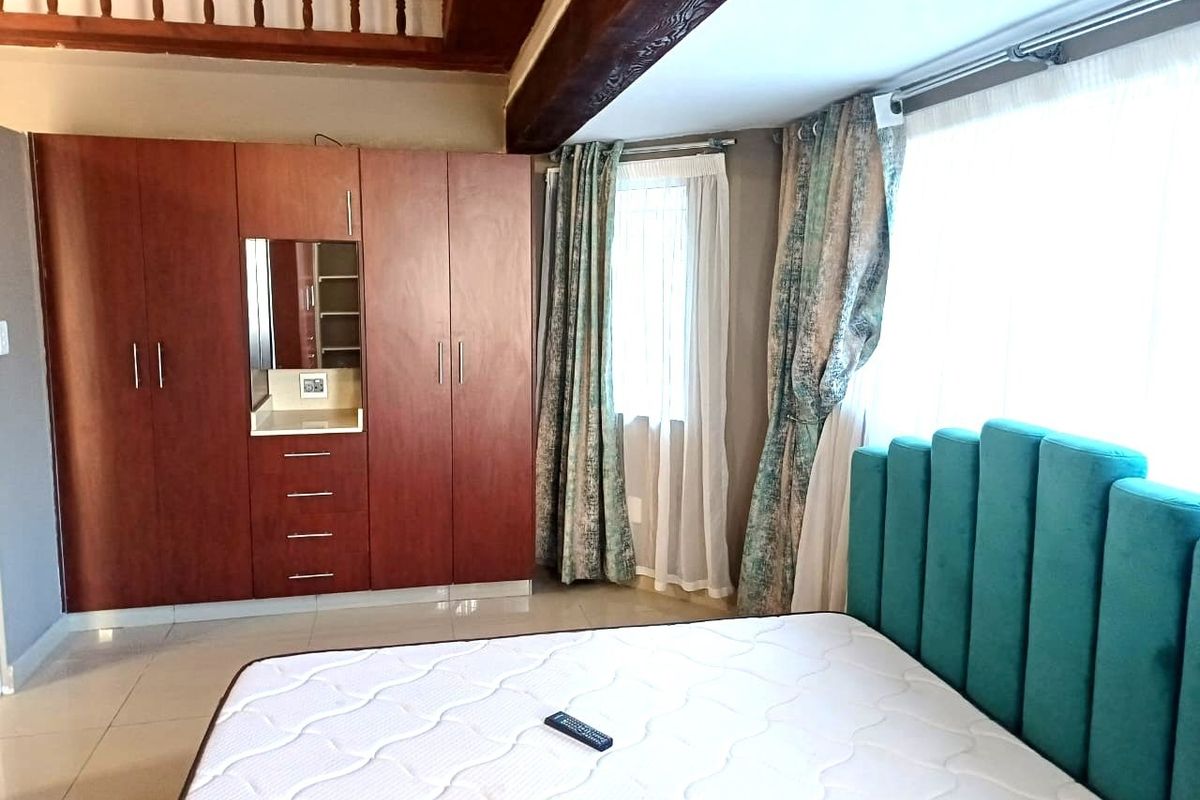 A well-maintained bedroom featuring built-in wooden cupboards, tiled flooring, and exposed timber ceiling beams, offering a cozy and functional living space.