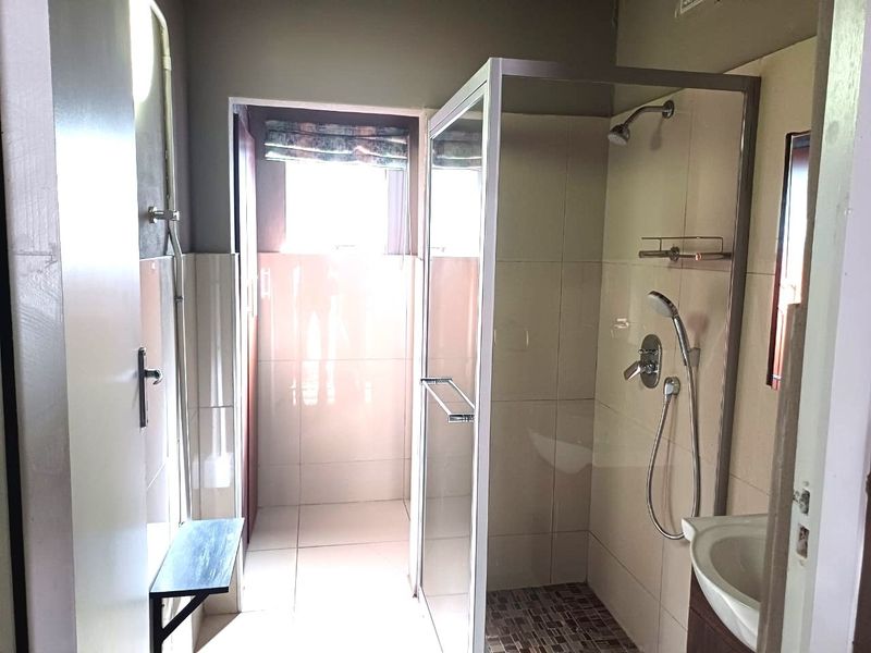 A functional bathroom featuring a glass-enclosed shower, tiled walls and flooring, and a vanity basin.