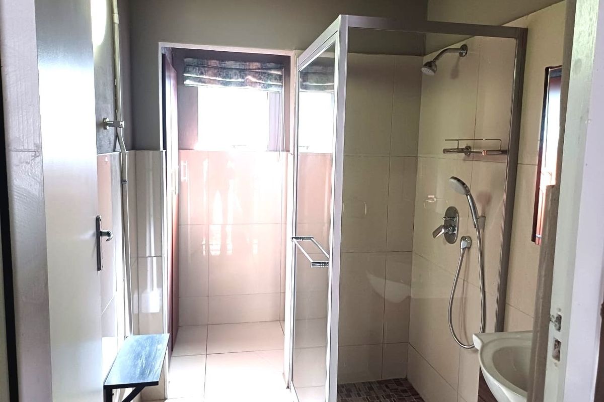 A functional bathroom featuring a glass-enclosed shower, tiled walls and flooring, and a vanity basin.