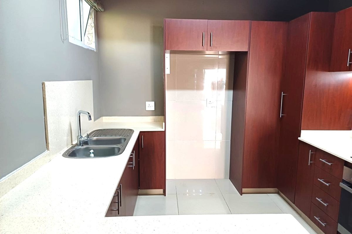 A clean, modern kitchen featuring dark wood cabinetry, light stone countertops, a double bowl sink, and tiled flooring.