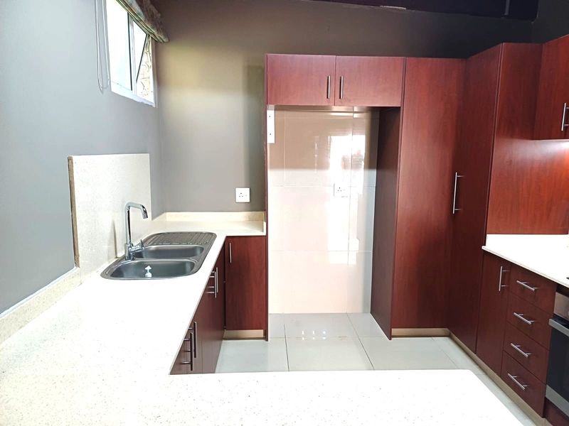 A clean, modern kitchen featuring dark wood cabinetry, light stone countertops, a double bowl sink, and tiled flooring.