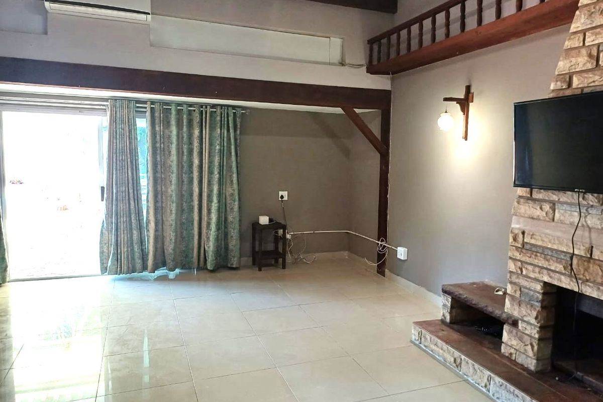 Spacious living room featuring a prominent stone fireplace, exposed timber beams, tiled flooring, and access to the outdoors via a sliding glass door.