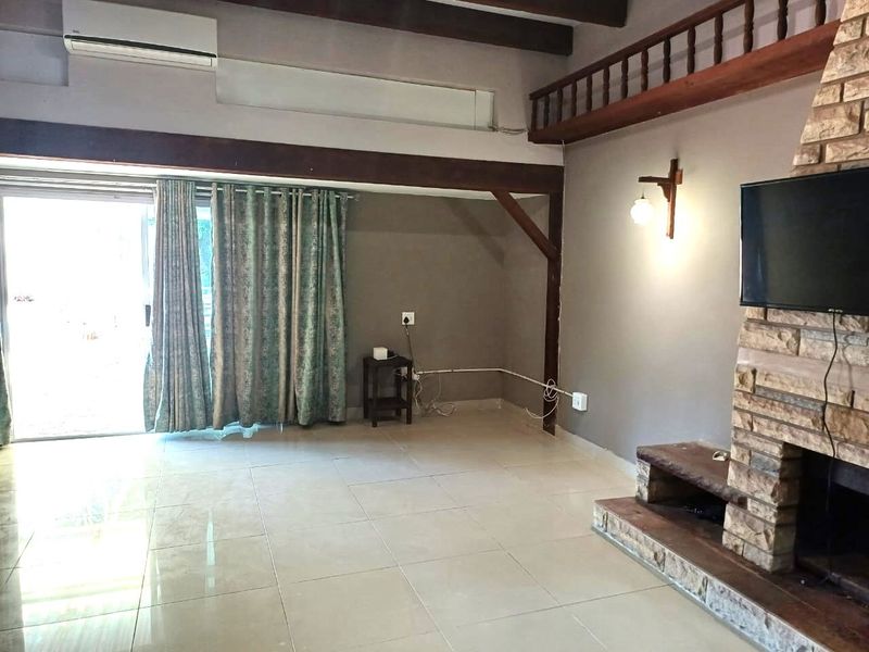 Spacious living room featuring a prominent stone fireplace, exposed timber beams, tiled flooring, and access to the outdoors via a sliding glass door.