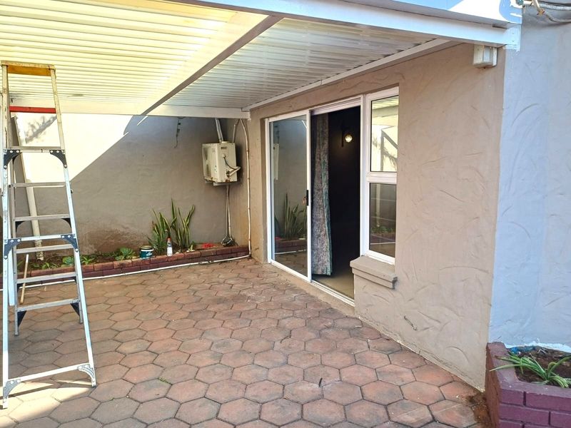 A covered patio area featuring paved flooring, a brick planter box, and a sliding glass door providing access to the interior.