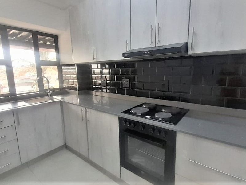 Modern kitchen featuring light-toned cabinetry, dark subway tile backsplash, stone countertops, and integrated appliances including an electric hob and oven.