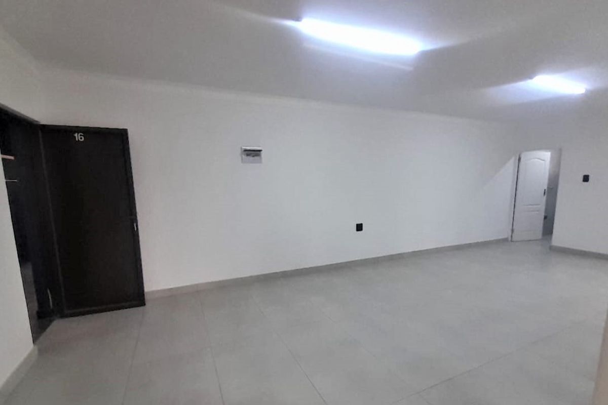 An empty, open-plan living area featuring neutral tiled flooring, white walls, and functional overhead lighting.