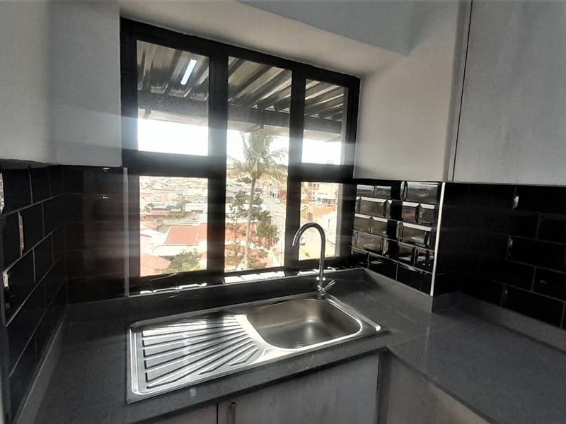 A modern kitchen area featuring a stainless steel sink, stone countertops, and sleek black subway tile backsplash with a view through the window.