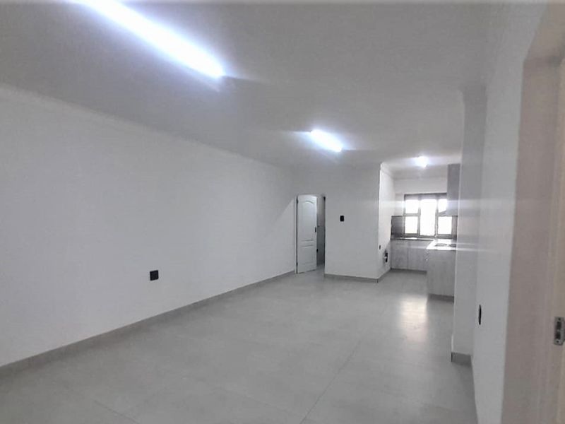 An open-plan living and kitchen area featuring neutral tiled flooring, white walls, and functional kitchen cabinetry in a bright, vacant space.