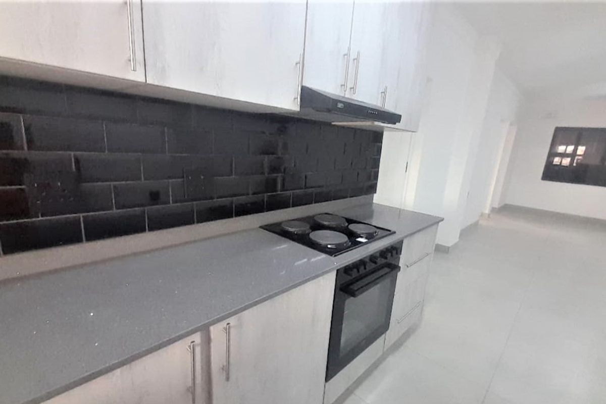 Modern kitchen featuring light-toned cabinetry, stone countertops, a black subway tile backsplash, and integrated electric cooking appliances.