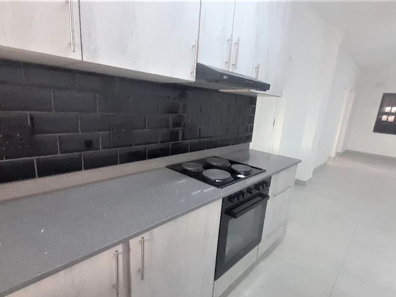 Modern kitchen featuring light-toned cabinetry, stone countertops, a black subway tile backsplash, and integrated electric cooking appliances.