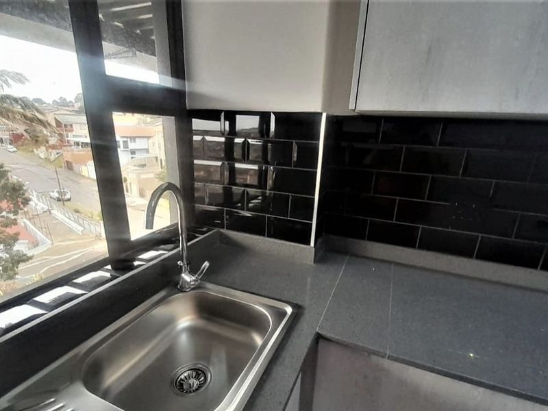 Modern kitchen area featuring a stainless steel sink, stone countertops, and a stylish black subway tile backsplash with large windows providing natural light.