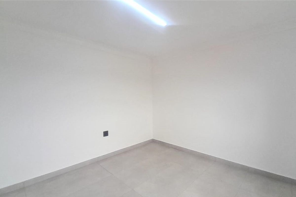A clean, empty bedroom featuring neutral tiled flooring and a simple ceiling light fixture, ready for personalization.