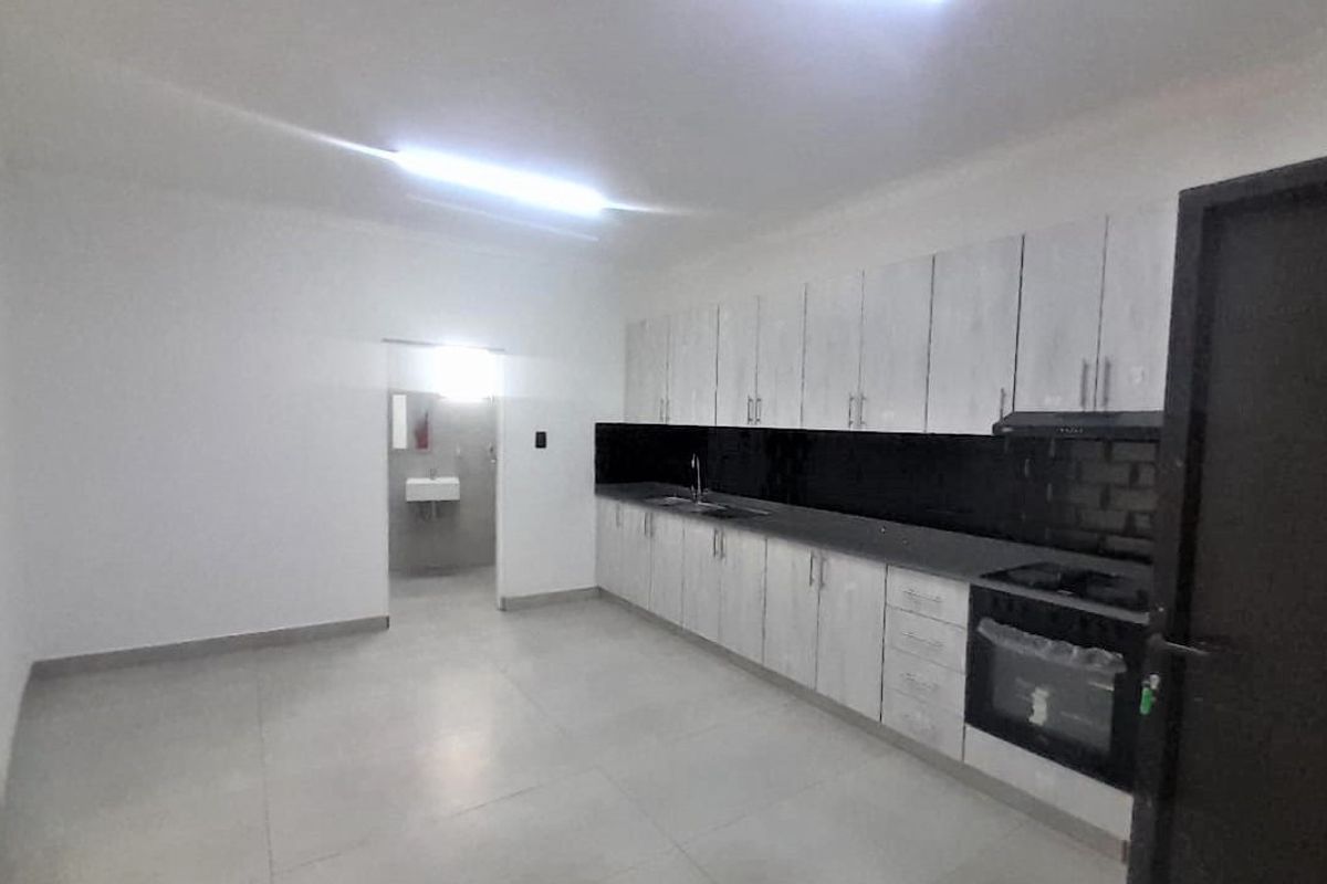 A clean, modern kitchen featuring light-toned built-in cabinetry, a contrasting black tiled backsplash, integrated oven, and hob with tiled flooring.