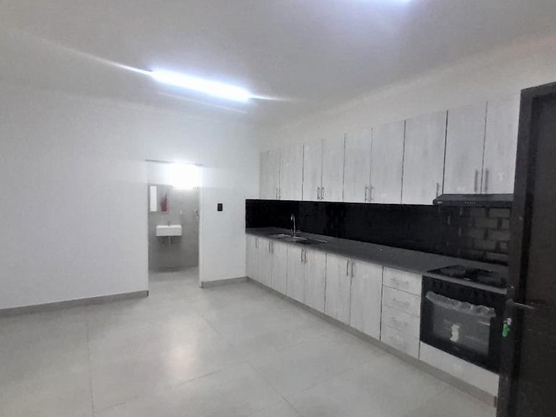 A clean, modern kitchen featuring light-toned built-in cabinetry, a contrasting black tiled backsplash, integrated oven, and hob with tiled flooring.
