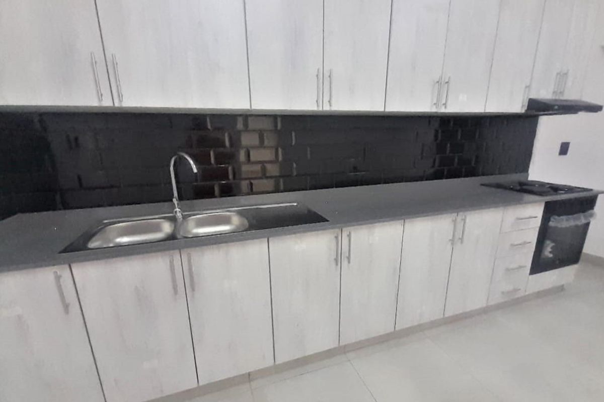 Modern kitchen featuring light wood-grain cabinetry, dark subway tile backsplash, stone countertops, and integrated oven with extractor fan.