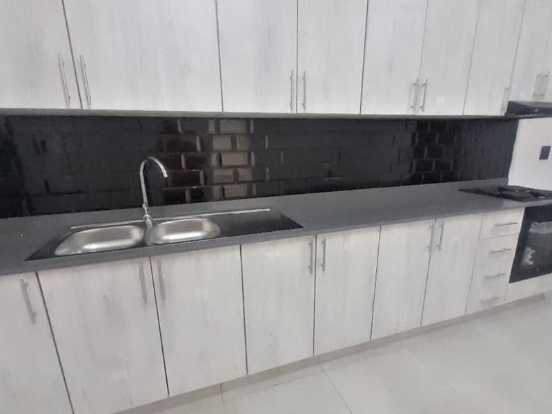 Modern kitchen featuring light wood-grain cabinetry, dark subway tile backsplash, stone countertops, and integrated oven with extractor fan.