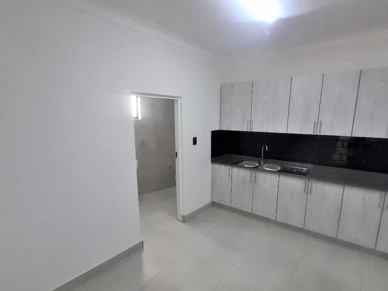 A clean, empty kitchen featuring white built-in cabinetry, a black splashback, and a double sink with tiled flooring.