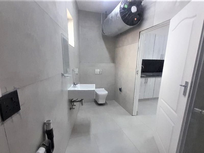 A partially finished bathroom featuring a wall-mounted basin, wall-hung toilet, and exposed water heater, requiring final touches to complete the installation.
