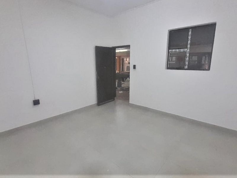An empty, neutral-toned bedroom featuring tiled flooring and an aluminium-framed window, providing a blank canvas for interior design.