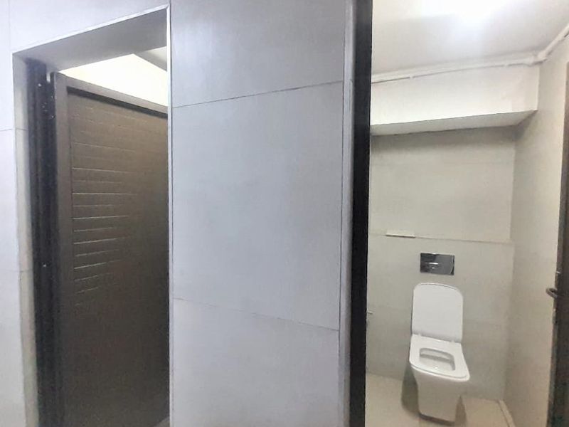 A functional bathroom featuring a wall-mounted toilet with a concealed cistern and neutral wall tiling.