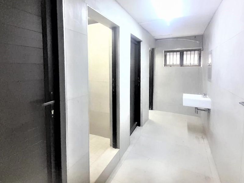 A minimalist hallway featuring tiled walls and flooring, a wall-mounted basin, and a window with security bars.