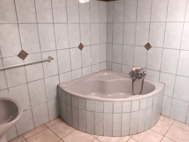 A dated bathroom featuring a corner bathtub with tiled surround and wall tiling, presenting an opportunity for modernization and renovation.