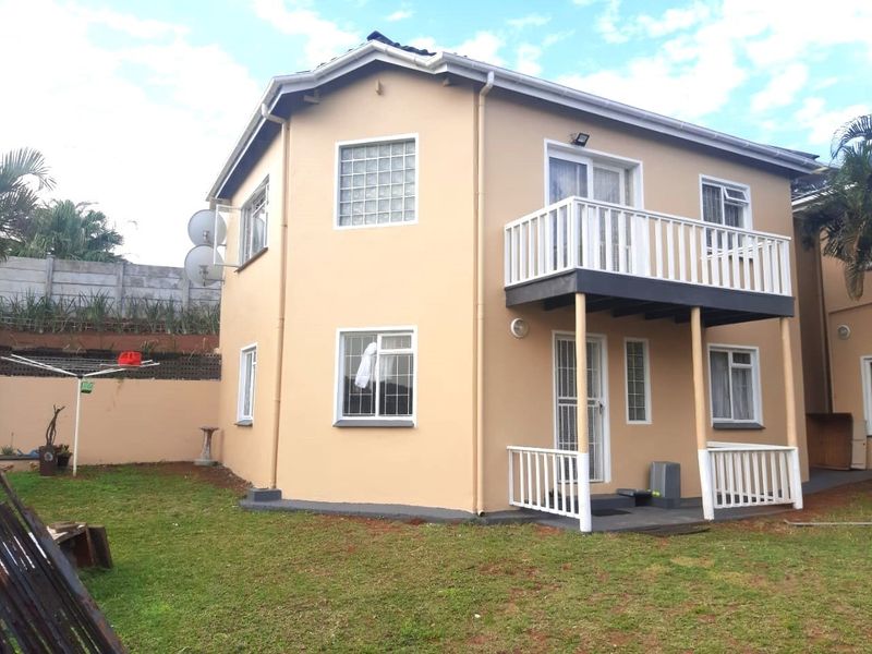 Rear view of a two-story cottage featuring a balcony with white railings, glass block windows, and a private garden area.
