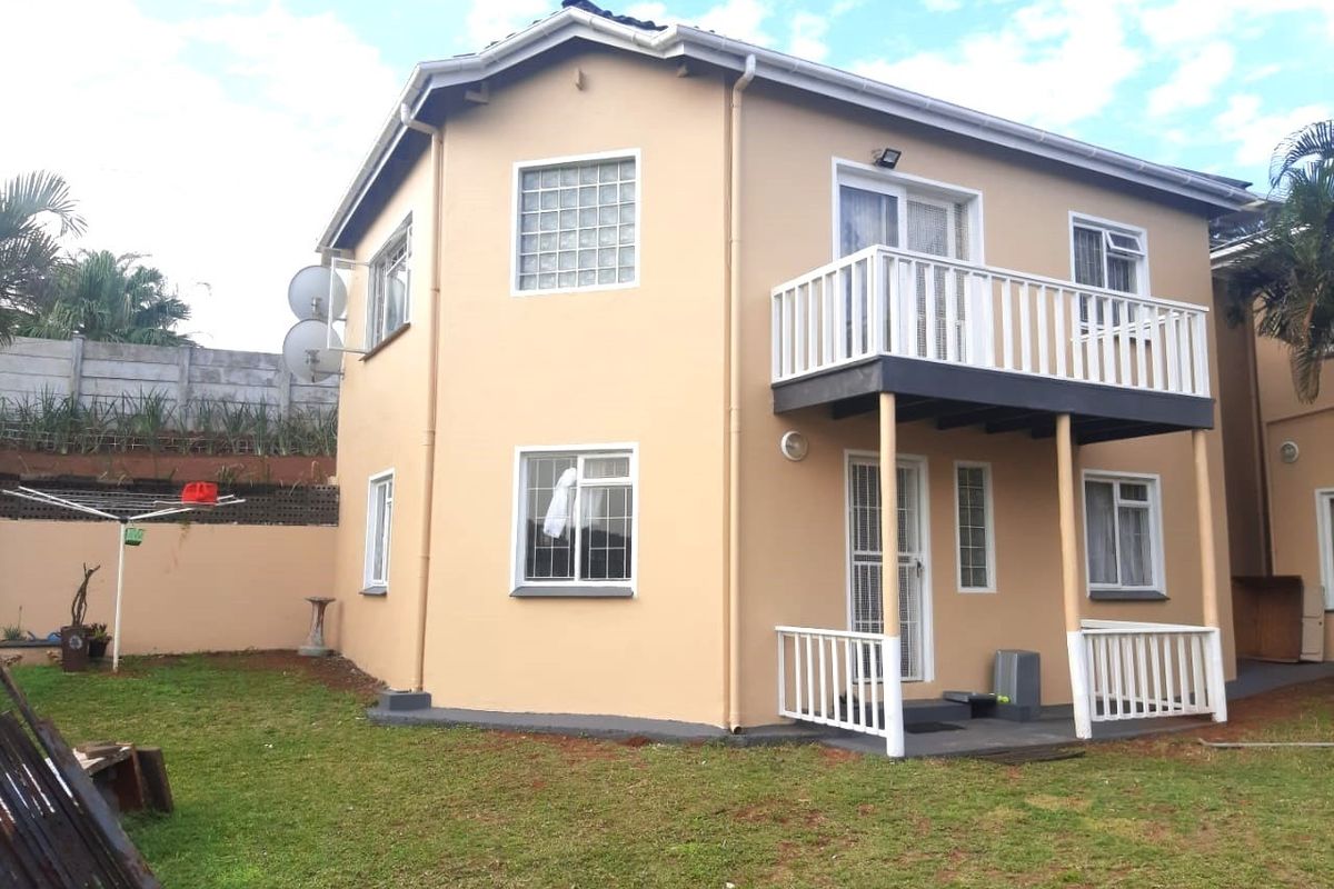 Rear view of a two-story cottage featuring a balcony with white railings, glass block windows, and a private garden area.