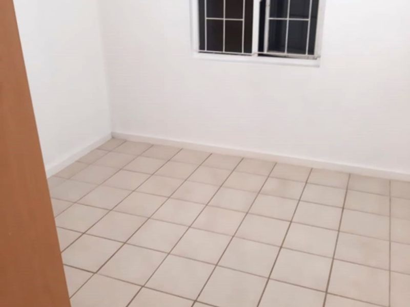 A clean, empty bedroom featuring neutral tiled flooring and a window fitted with security bars.