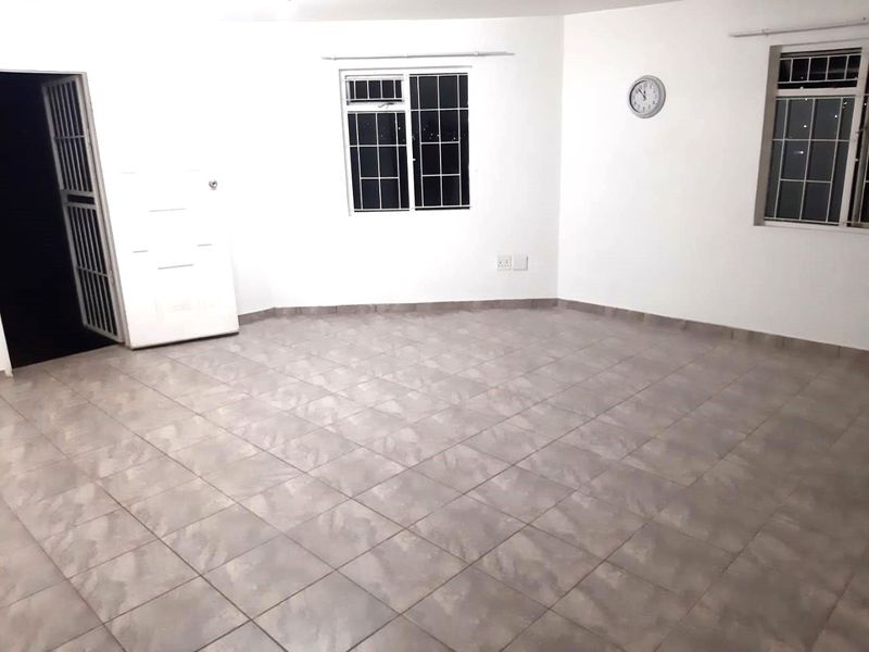 A spacious, empty living area featuring neutral tiled flooring, security bars on the windows, and a secure entrance gate.