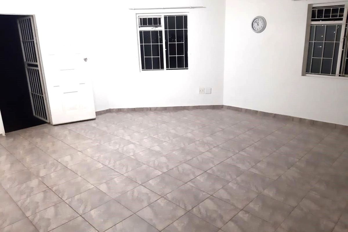 A spacious, empty living area featuring neutral tiled flooring, security bars on the windows, and a secure entrance gate.