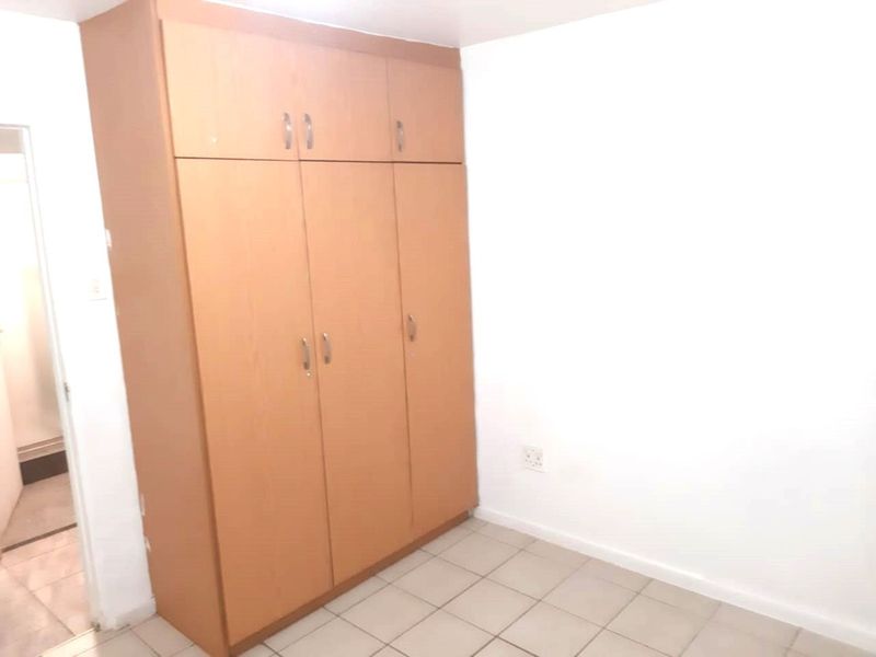 A clean, empty bedroom featuring neutral tiled flooring and a large, functional built-in wooden wardrobe with overhead storage compartments.