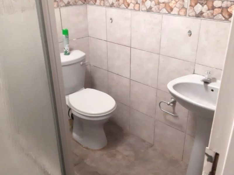 A functional bathroom featuring a pedestal basin, toilet, and a shower enclosure with tiled walls and flooring.